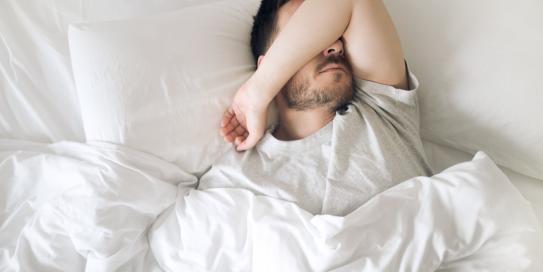 Mann im Bett hält Arm vor Gesicht